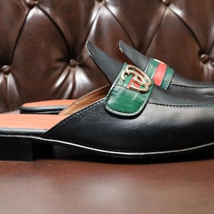 High-quality black leather loafers with a green and red webbed strap.