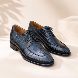 Peut inclure: Une paire de chaussures de ville en cuir noir avec un motif texturé en forme de crocodile. Les chaussures ont un design classique à lacets et un petit talon. La doublure intérieure est de couleur marron clair.