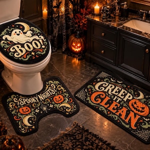 Op de afbeelding: Een driedelige badkamerset bestaande uit een zwarte toiletbrilhoes met een witte geest en de tekst BOO!, een U-vormig matje met de tekst SPOOKY NIGHTS en een rechthoekig matje met de tekst CREEP IT CLEAN, allemaal versierd met oranje pompoenen.