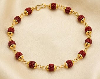 May include: A gold chain bracelet featuring twelve round, textured dark red beads. Each bead is flanked by small gold caps and connected by gold circular links. The bracelet includes a gold hook-style clasp at the top for secure closure.