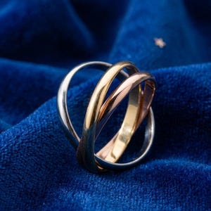 Peut inclure: Une bague trois anneaux entrelacés composée de trois bandes mobiles aux tons argenté, or jaune et or rose. Les anneaux métalliques lisses et arrondis sont reliés dans une conception en boucle continue, créant un aspect superposé avec une finition brillante.