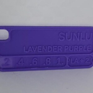 K&ouml;nnte beinhalten: Ein lavendelfarbener Kunststoff-Farbmuster mit abgerundeten Kanten. Der Text "SUNLU LAVENDER PURPLE" ist auf der Oberfl&auml;che aufgedruckt, zusammen mit Zahlen und "PLA + 2.0". Das Muster hat oben ein kleines Loch.