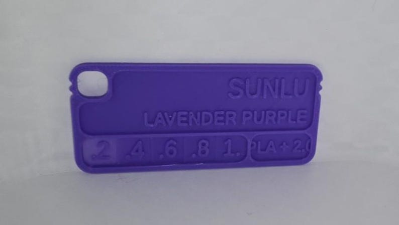 K&ouml;nnte beinhalten: Ein lavendelfarbener Kunststoff-Farbmuster mit abgerundeten Kanten. Der Text "SUNLU LAVENDER PURPLE" ist auf der Oberfl&auml;che aufgedruckt, zusammen mit Zahlen und "PLA + 2.0". Das Muster hat oben ein kleines Loch.