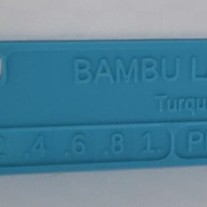 K&ouml;nnte beinhalten: Ein t&uuml;rkisfarbenes Kunststoff-Farbmuster von Bambu Lab. Das Muster tr&auml;gt den Text "BAMBU LAB Turquoise" und die Zahlen 2, 4, 6, 8, 1 und PLA. Es hat ein Loch auf der linken Seite.
