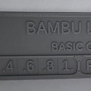 K&ouml;nnte beinhalten: Ein graues 3D-gedrucktes Farbmuster von Bambu Lab, beschriftet mit "Basic Gray". Das Muster enth&auml;lt Zahlen von .2 bis 1.0 und die Buchstaben "PLA". Der Artikel hat einen Ausschnitt auf der linken Seite.