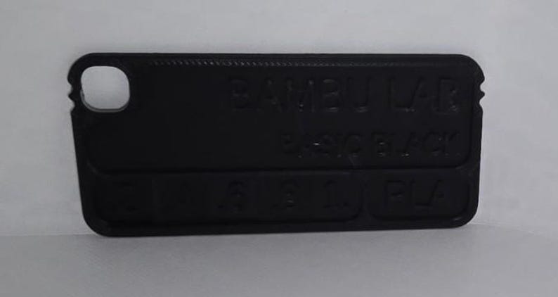 K&ouml;nnte beinhalten: Eine schwarze, rechteckige Handyh&uuml;lle mit abgerundeten Ecken. Die H&uuml;lle hat einen Ausschnitt f&uuml;r ein Kameraobjektiv und tr&auml;gt den gepr&auml;gten Text "BAMBU LAB", "BASIC BLACK" und "PLA".