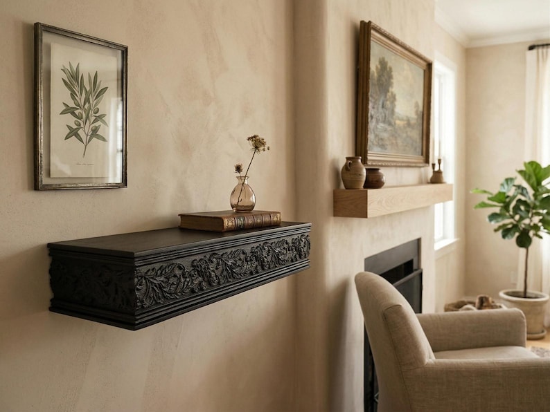 May include: A dark, carved wooden shelf with floral detailing is fixed to a beige wall. A framed botanical print and a small glass vase with dried flowers are placed above the shelf. A framed painting hangs on the wall.