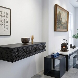 May include: An interior scene with a dark wood floating shelf with carved floral details, holding a decorative bowl and glass. A framed Japanese print hangs above. A table with a tea set, two black cube stools, and a bonsai tree are also present.