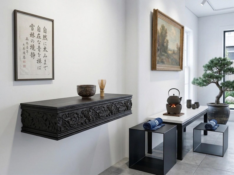 May include: An interior scene with a dark wood floating shelf with carved floral details, holding a decorative bowl and glass. A framed Japanese print hangs above. A table with a tea set, two black cube stools, and a bonsai tree are also present.
