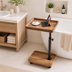 May include: A mobile side table with a dark wood grain finish, featuring a rectangular top and base connected by a black adjustable metal post. The table is equipped with small wheels and holds a white coffee cup on a saucer and a tablet computer.