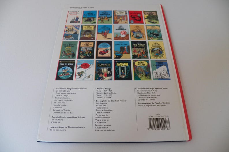 May include: A white back cover of a Tintin book featuring a grid of twenty-four colorful comic book cover illustrations. Below the grid, there are three columns of black text listing various titles and a barcode with the ISBN 2-203-00118-9.