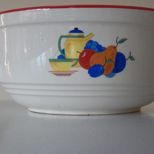 Könnte beinhalten: Weiße Keramik-Rührschüssel mit rotem Rand und einem farbenfrohen Obst- und Teekannen-Design. Die Schüssel zeigt eine dekorative Illustration einer gelben Teekanne, einer Tasse und verschiedenen Früchten, darunter Äpfel, Birnen und Pflaumen.