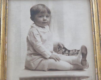 Fotografía antigua enmarcada de un niño pequeño con un caballo de juguete, marca Foster Bros. Boston. Marco dorado.