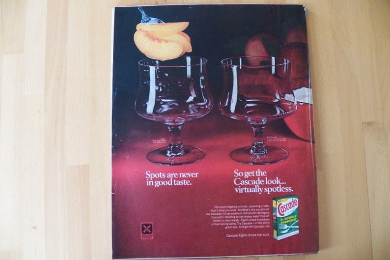 May include: An advertisement featuring two clear stemmed glasses with a peach and water droplets above them. The text reads "Spots are never in good taste" and "So get the Cascade look... virtually spotless."