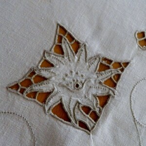May include: White linen tablecloth with delicate embroidered floral designs. The tablecloth features a large, intricate flower in the center and smaller floral motifs around the edges.