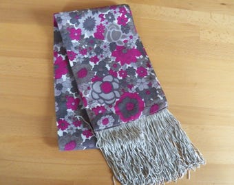May include: A grey and pink floral patterned scarf with a fringe on the bottom edge.