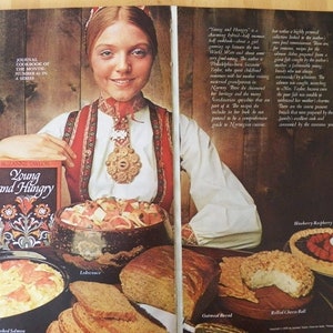 May include: An advertisement for a cookbook titled "Young and Hungry" featuring a woman in traditional Norwegian attire. The image showcases various dishes, including scrambled eggs with smoked salmon, bread, and a berry tart.