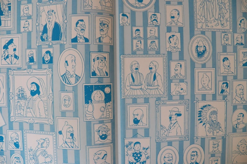 May include: A wallpaper pattern featuring a light blue and white vertical striped background covered in numerous framed illustrations of various characters in a blue ink line art style, including portraits, figures in hats, and a space-suited character.