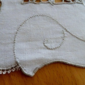 May include: A white linen tablecloth with a scalloped edge and delicate embroidered details. The embroidery features a repeating pattern of swirls and loops.
