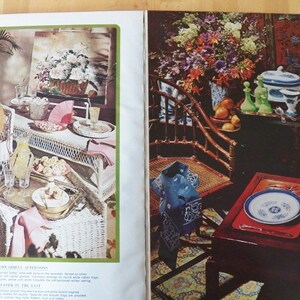 May include: A vintage magazine spread featuring two interior scenes. One shows a wicker chair and table set with a hat, fan, and refreshments. The other depicts a table set with china, glassware, and flowers.
