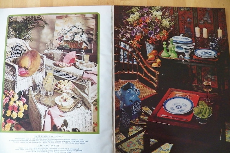 May include: A vintage magazine spread featuring two interior scenes. One shows a wicker chair and table set with a hat, fan, and refreshments. The other depicts a table set with china, glassware, and flowers.