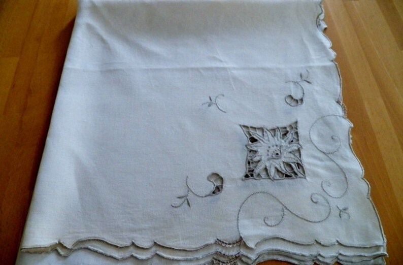 May include: White linen tablecloth with delicate embroidered floral designs and scalloped edges.