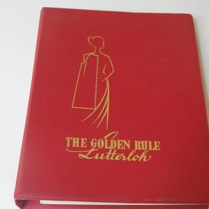 May include: Red book with gold lettering and a stylized illustration of a person wearing a long coat. The text reads "THE GOLDEN RULE Lutterloh". The book appears to be a pattern book or guide.