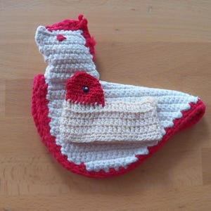 Puede incluir: Un agarrador de ganchillo hecho a mano con forma de gallina en blanco, rojo y beige. El agarrador presenta una cresta y un pico rojos, con un cuerpo beige y alas blancas. Los bordes están ribeteados en rojo.