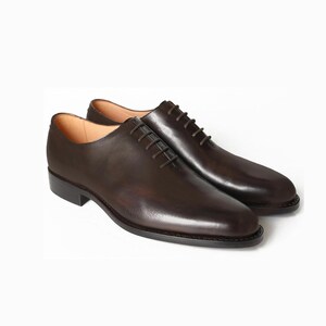 May include: A pair of brown leather dress shoes with a classic Oxford design. The shoes feature a polished finish, a lace-up closure, and a low heel. The leather has a rich, dark brown color, and the shoes are set against a white background.