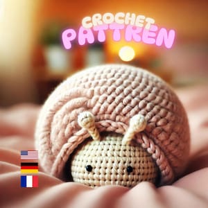 Könnte beinhalten: Ein gehäkeltes Schneckenspielzeug mit einem großen, strukturierten, altrosa Gehäuse und einem cremefarbenen Kopf mit zwei kleinen Fühlern und zwei schwarzen Perlenaugen. Der Text CROCHET PATTREN steht in hellrosa Buchstaben über der Figur.