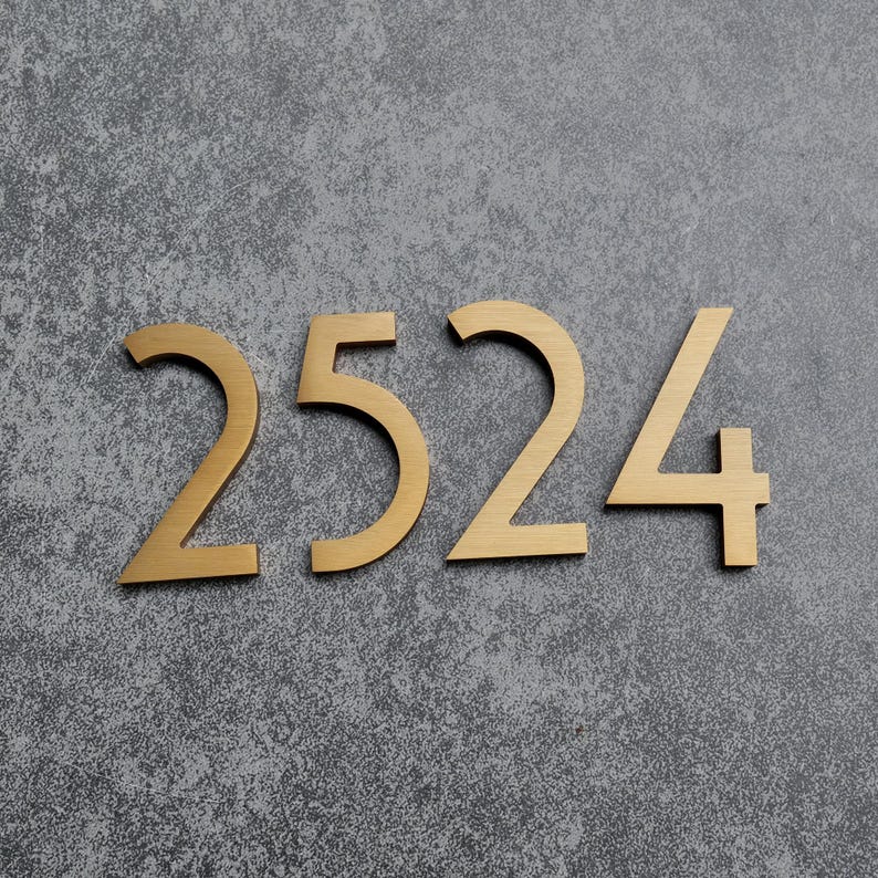 May include: A set of four individual house numbers forming the sequence 2524, crafted from a brushed gold-toned metal with a smooth finish. Each digit features a clean, sans-serif typeface with sharp, angular lines and a flat, uniform surface.