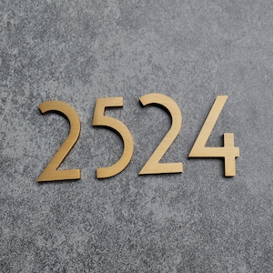 May include: A set of four individual house numbers forming the sequence 2524, crafted from a brushed gold-toned metal with a smooth finish. Each digit features a clean, sans-serif typeface with sharp, angular lines and a flat, uniform surface.