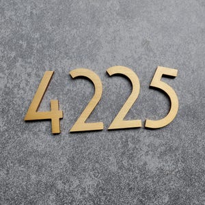 May include: Four individual house numbers forming the sequence 4225, crafted from a brushed gold-toned metal with a smooth finish. Each digit features a clean, sans-serif typeface with sharp, angular edges, presented in a horizontal arrangement.
