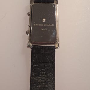 Puede incluir: Un reloj de pulsera rectangular con una correa de cuero negro. La esfera del reloj es plateada con una correa de cuero negro. La parte trasera del reloj es visible, con el texto "STAINLESS STEEL BACK" y el n&uacute;mero "94201".