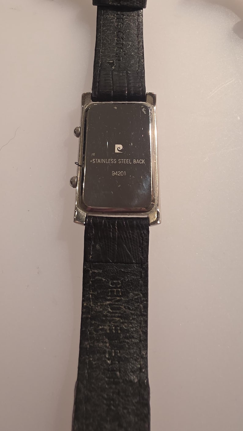 Puede incluir: Un reloj de pulsera rectangular con una correa de cuero negro. La esfera del reloj es plateada con una correa de cuero negro. La parte trasera del reloj es visible, con el texto "STAINLESS STEEL BACK" y el n&uacute;mero "94201".