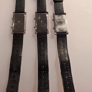 Puede incluir: Tres relojes de pulsera con correas de cuero negro y esferas rectangulares plateadas. Las correas de los relojes son texturizadas y tienen hebillas plateadas. Las esferas de los relojes tienen la marca "Pierre Cardin" y "Stainless Steel Back".