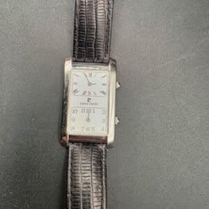Puede incluir: Un reloj rectangular plateado Pierre Cardin con esfera blanca y n&uacute;meros romanos negros. El reloj tiene una correa de cuero negro. La esfera muestra la hora y el logotipo de Pierre Cardin.