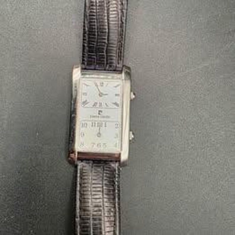 Puede incluir: Un reloj rectangular plateado Pierre Cardin con esfera blanca y n&uacute;meros romanos negros. El reloj tiene una correa de cuero negro. La esfera muestra la hora y el logotipo de Pierre Cardin.