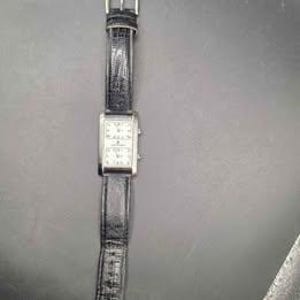 Puede incluir: Un reloj de pulsera rectangular con esfera plateada y correa de cuero negro. La esfera del reloj est&aacute; dividida en dos secciones, cada una mostrando una esfera de reloj. La correa tiene un cierre de hebilla.