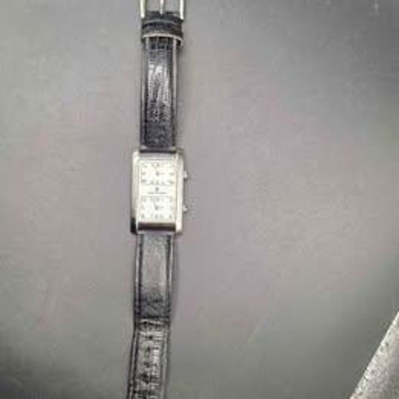 Puede incluir: Un reloj de pulsera rectangular con esfera plateada y correa de cuero negro. La esfera del reloj est&aacute; dividida en dos secciones, cada una mostrando una esfera de reloj. La correa tiene un cierre de hebilla.
