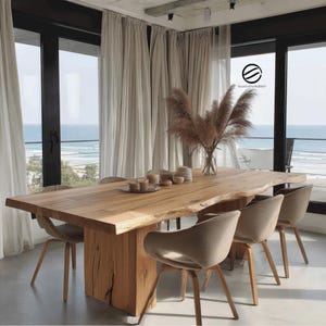 Peut inclure: Une grande table à manger en bois naturel avec un bord brut, accompagnée de six chaises rembourrées. La table repose sur un socle en bois massif. Un vase d'herbes ornementales séchées est au centre. La pièce a de grandes fenêtres avec vue sur la mer. La table mesure environ 240 cm de long.