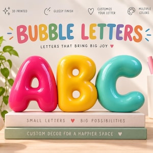 May include: Three 3D printed bubble letters A, B, and C with a glossy finish. The letter A is hot pink, B is yellow, and C is turquoise. They are displayed on two stacked books with the text "SMALL LETTERS BIG POSSIBILITIES" and "CUSTOM DECOR FOR A HAPPIER SPACE".