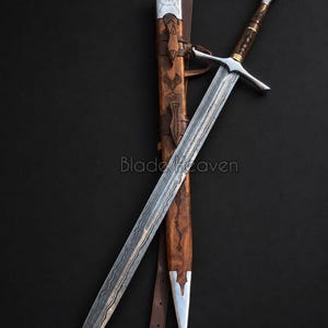 May include: A double-edged steel sword with a wavy pattern along the blade, a silver crossguard, and a brown wooden handle. It is accompanied by a matching brown wooden scabbard featuring silver metal accents and a brown leather belt strap.