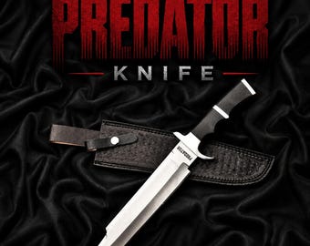May include: A fixed-blade knife with a silver-toned steel blade and a black handle, featuring the word PREDATOR engraved on the blade. The knife is accompanied by a black textured sheath with a snap closure, set against a black fabric background.