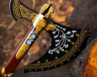 May include: A double-bitted axe featuring a dark brown wooden handle and a black metal head. The axe head is decorated with gold-colored filigree, white runic symbols, and geometric patterns. The handle includes gold-colored metal accents.