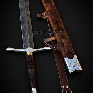 May include: A Damascus steel sword with a dark, wavy pattern on the blade, a wooden handle with intricate black carvings, gold-colored rings, and a silver pommel. It includes a matching wooden scabbard with leather straps and silver accents.