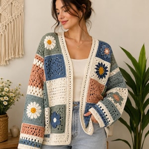 May include: A long-sleeved open-front cardigan constructed from various crocheted granny squares. The garment features a mix of muted blue, sage green, dusty pink, and cream yarn, with several squares displaying raised white and yellow daisy motifs.
