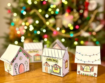 May include: Four paper houses decorated for Christmas. The houses are white with colorful details. One house is a coffee shop with a sign that says "Coffee Shop". Another house has a string of lights and a window with a candy cane design. The houses are sitting on a wooden table.