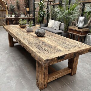 May include: A large, rectangular wooden table with a rustic, weathered appearance. The table is supported by thick, sturdy legs and has a natural wood grain. The table is approximately 244 cm long, suitable for a dining or living room.