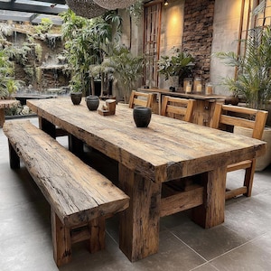 May include: A large, rustic wooden dining table with a matching bench and chairs. The table is made of reclaimed wood, with visible knots and grain. The table is approximately 305 cm long, and the bench is about 183 cm long. The chairs are also made of wood.